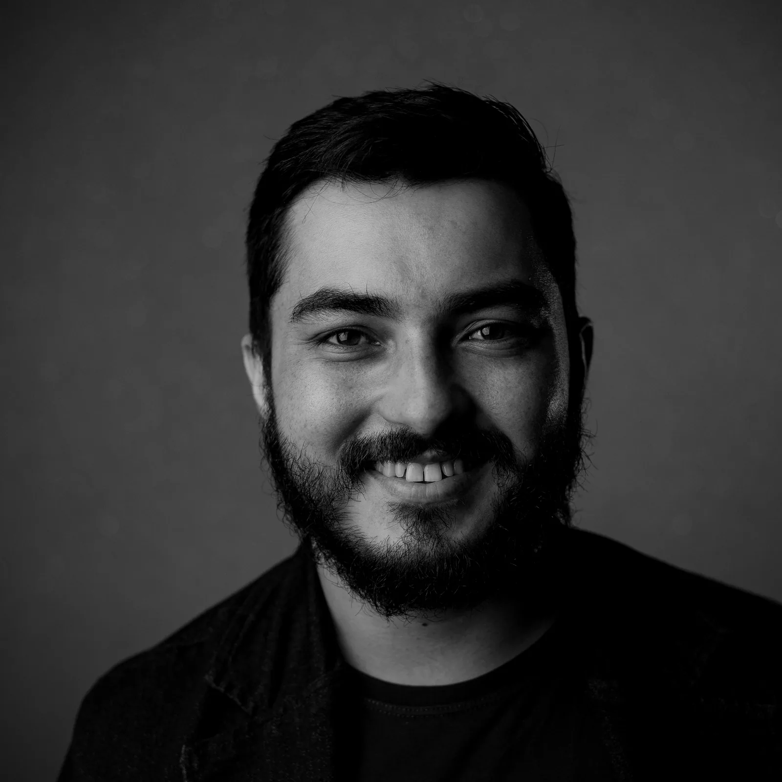 Hombre sonriendo tras su tratamiento dental, retrato en blanco y negro sobre fondo gris