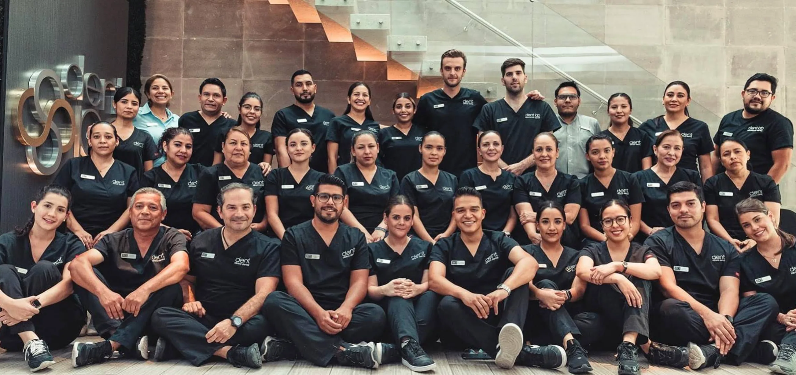 El equipo completo de Dent Clínica Dental frente al muro con el logotipo de la clínica